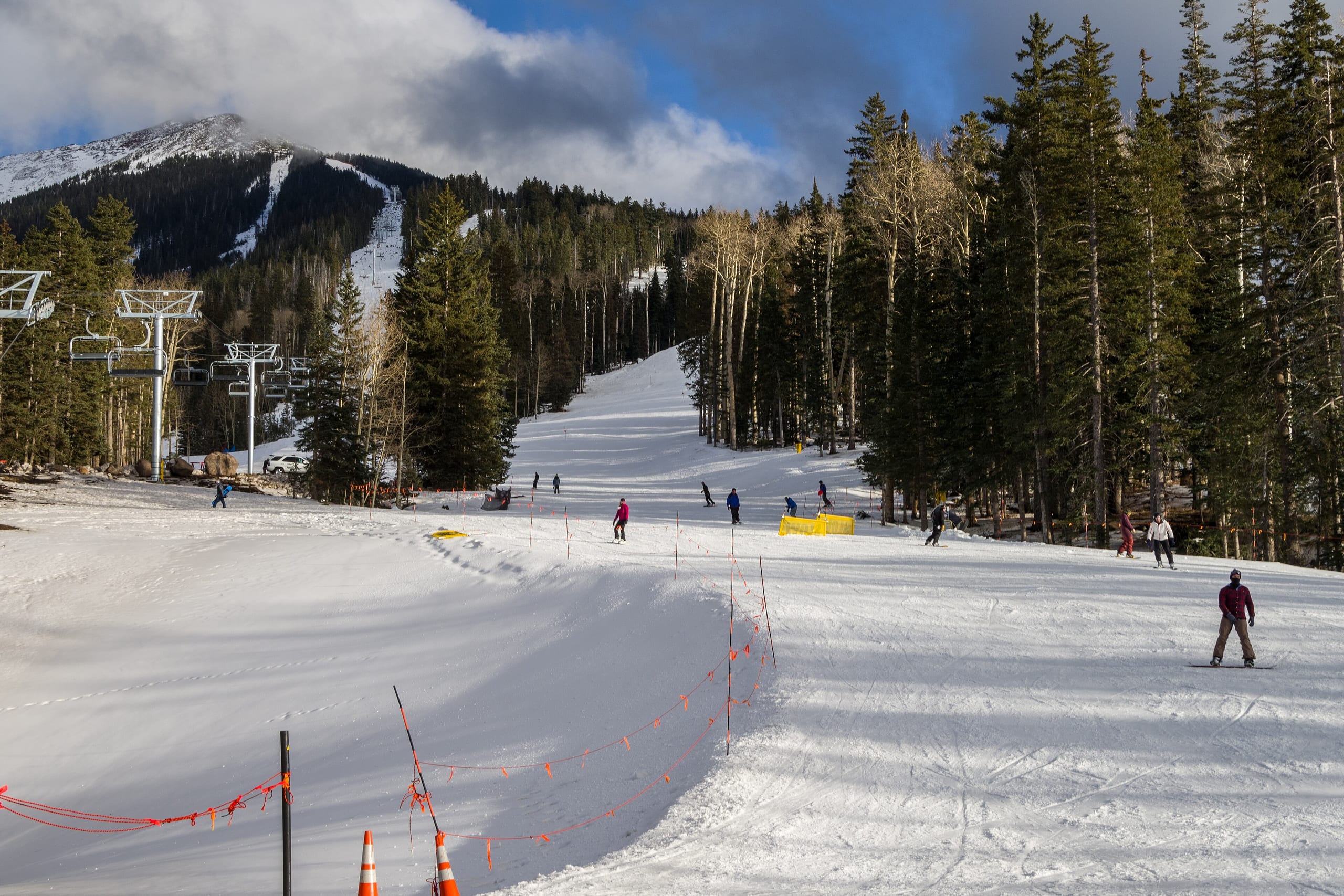 Skiers on a groomed run at Arizona Snowbowl with a chairlift and San Francisco Peaks behind