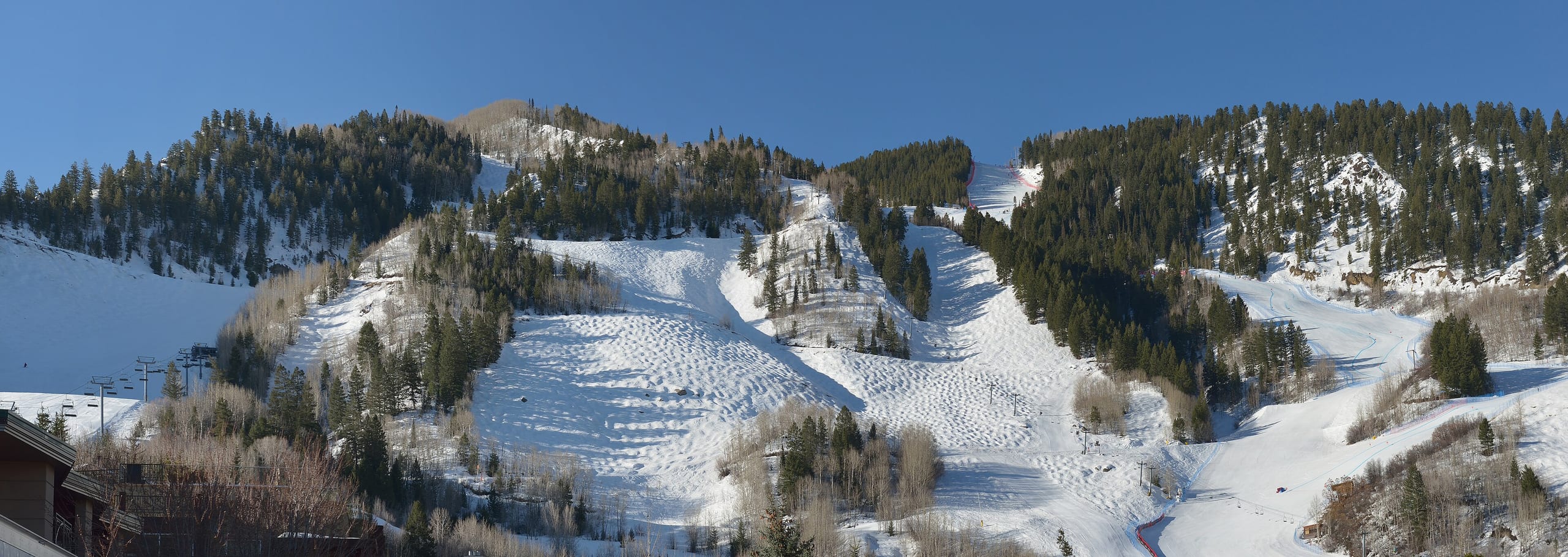 Snow-covered ski runs and moguls on a tree-lined mountain face above a chairlift near the base.