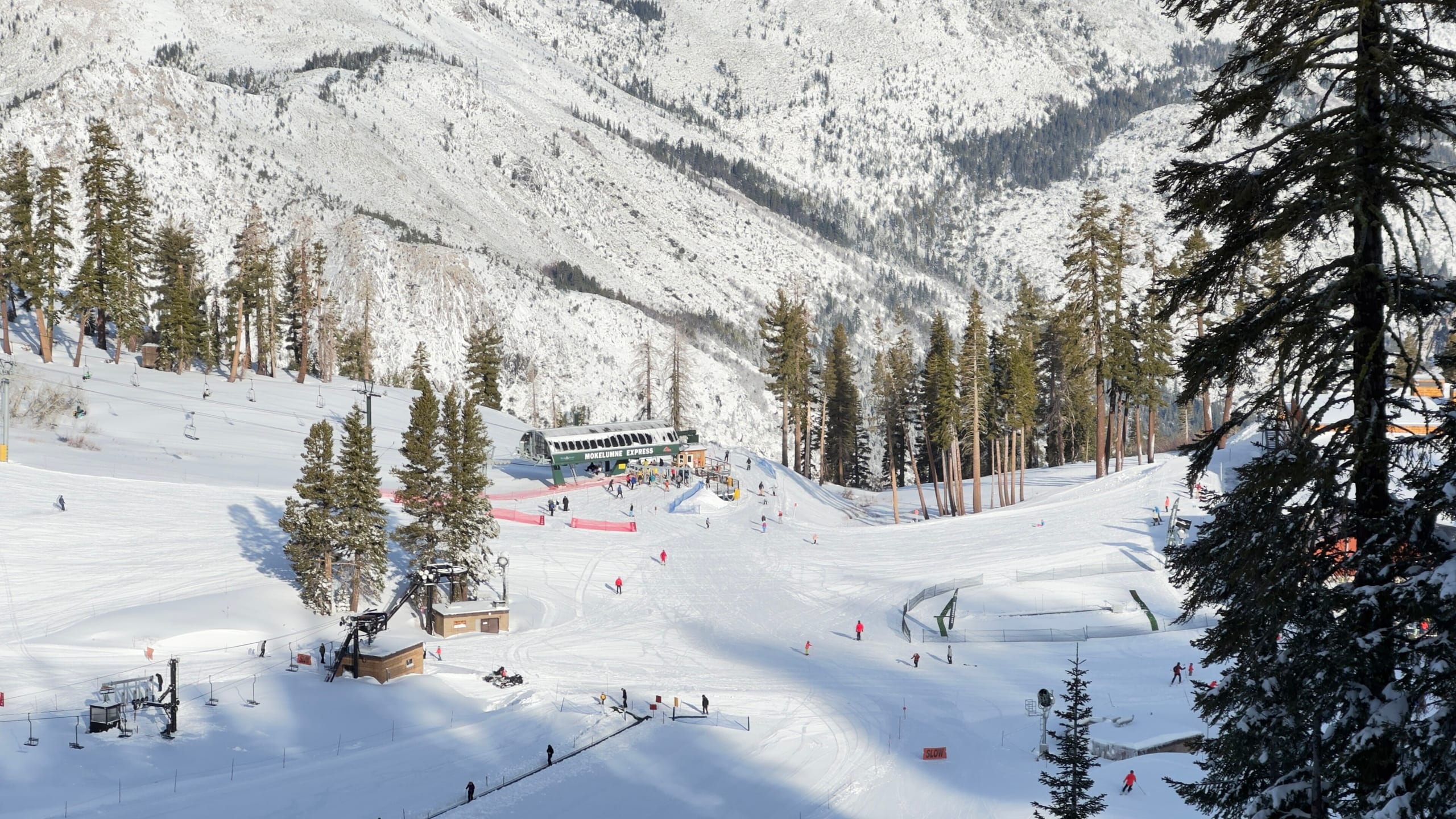 Snow-covered beginner slopes, a chairlift and a lodge below forested ridges at a ski area