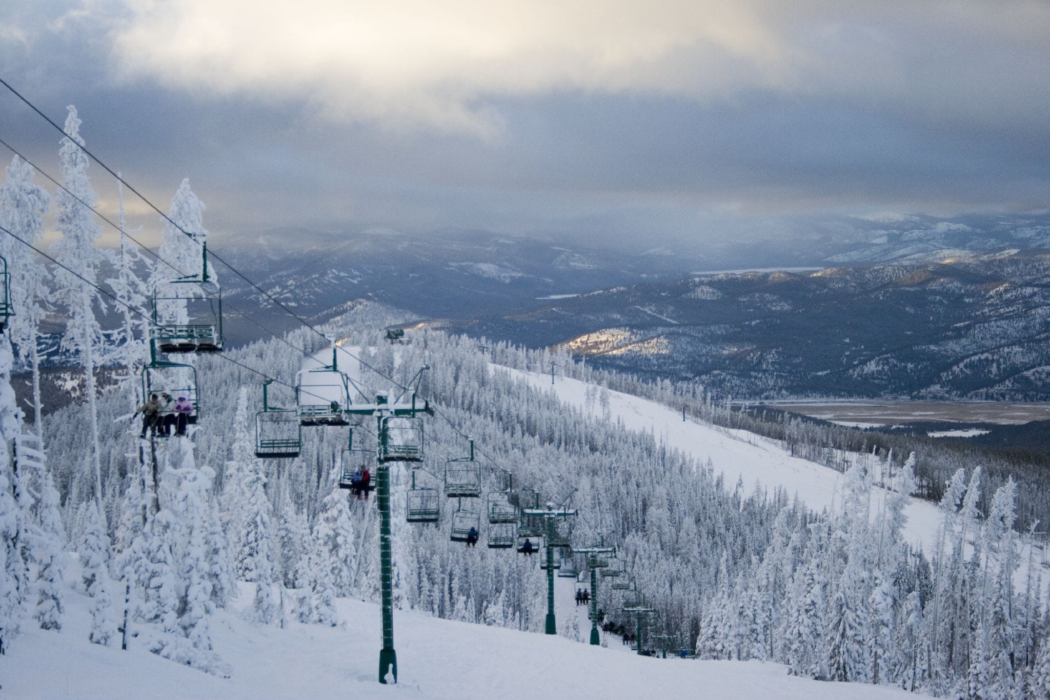 Chairlift rising past snow-covered trees on a ski slope with a wide valley below