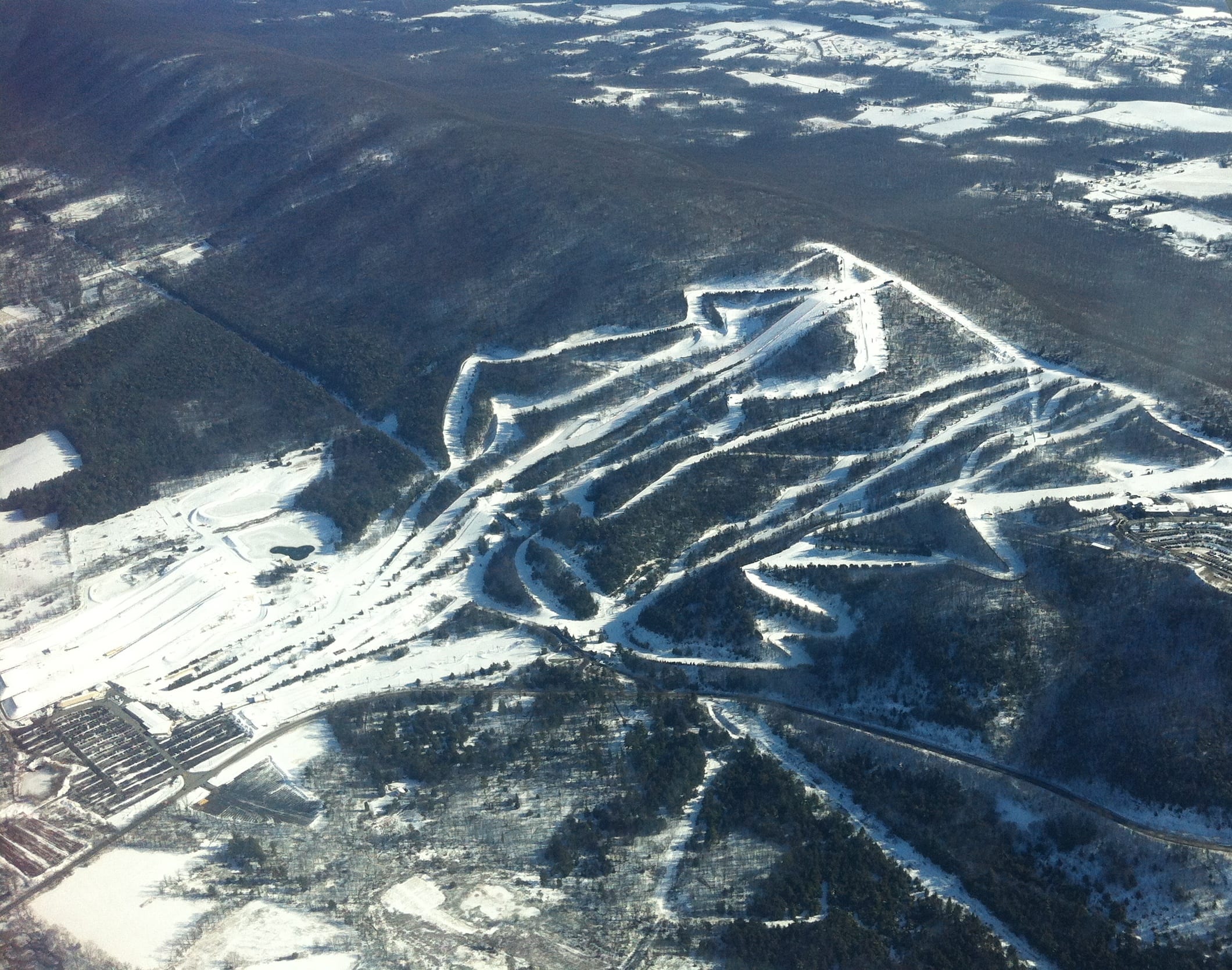 Aerial view of Blue Mountain ski area's snow-covered trail network and lifts on a forested ridge in winter.