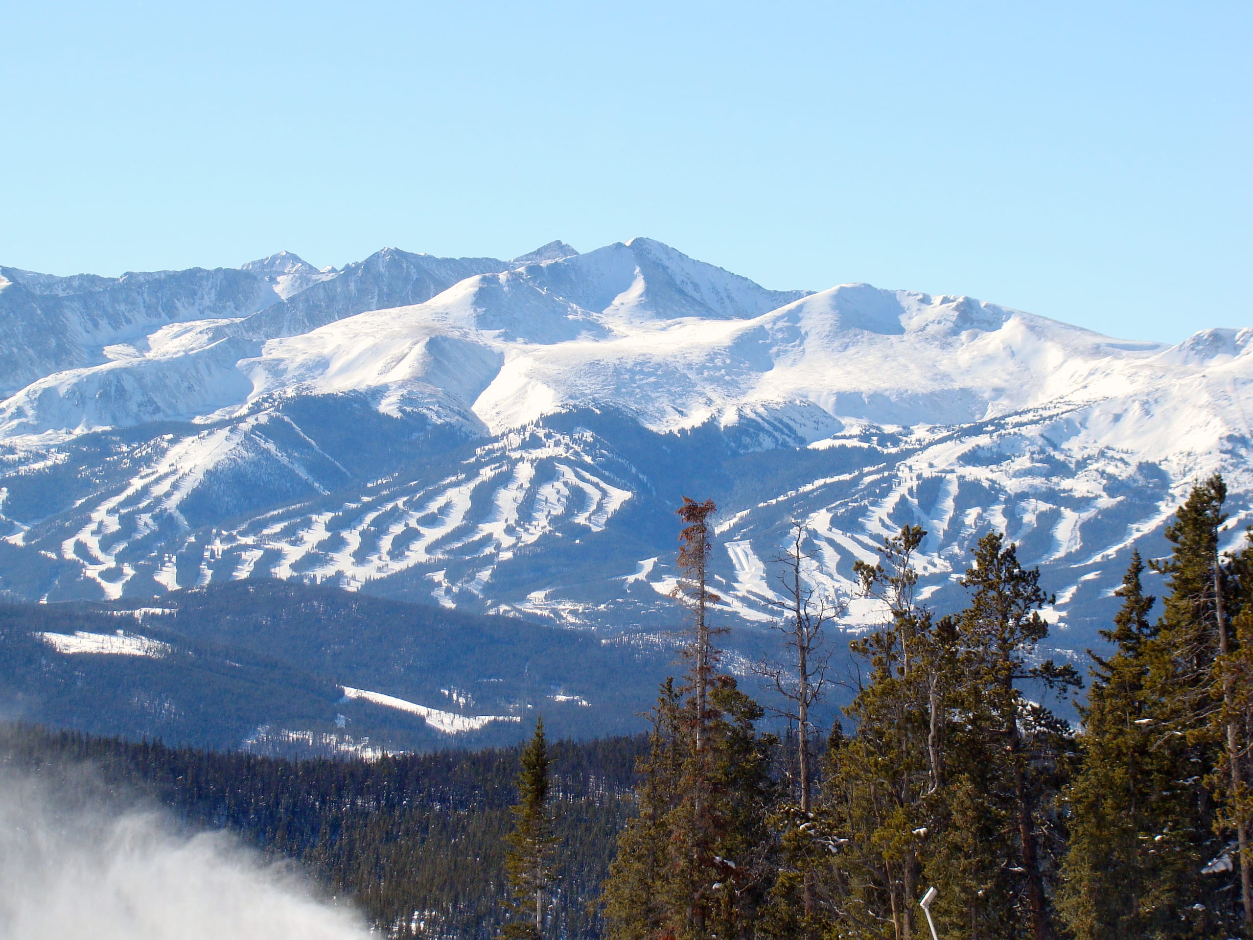 Snow-covered Breckenridge ski runs and peaks seen across a forested valley from Keystone