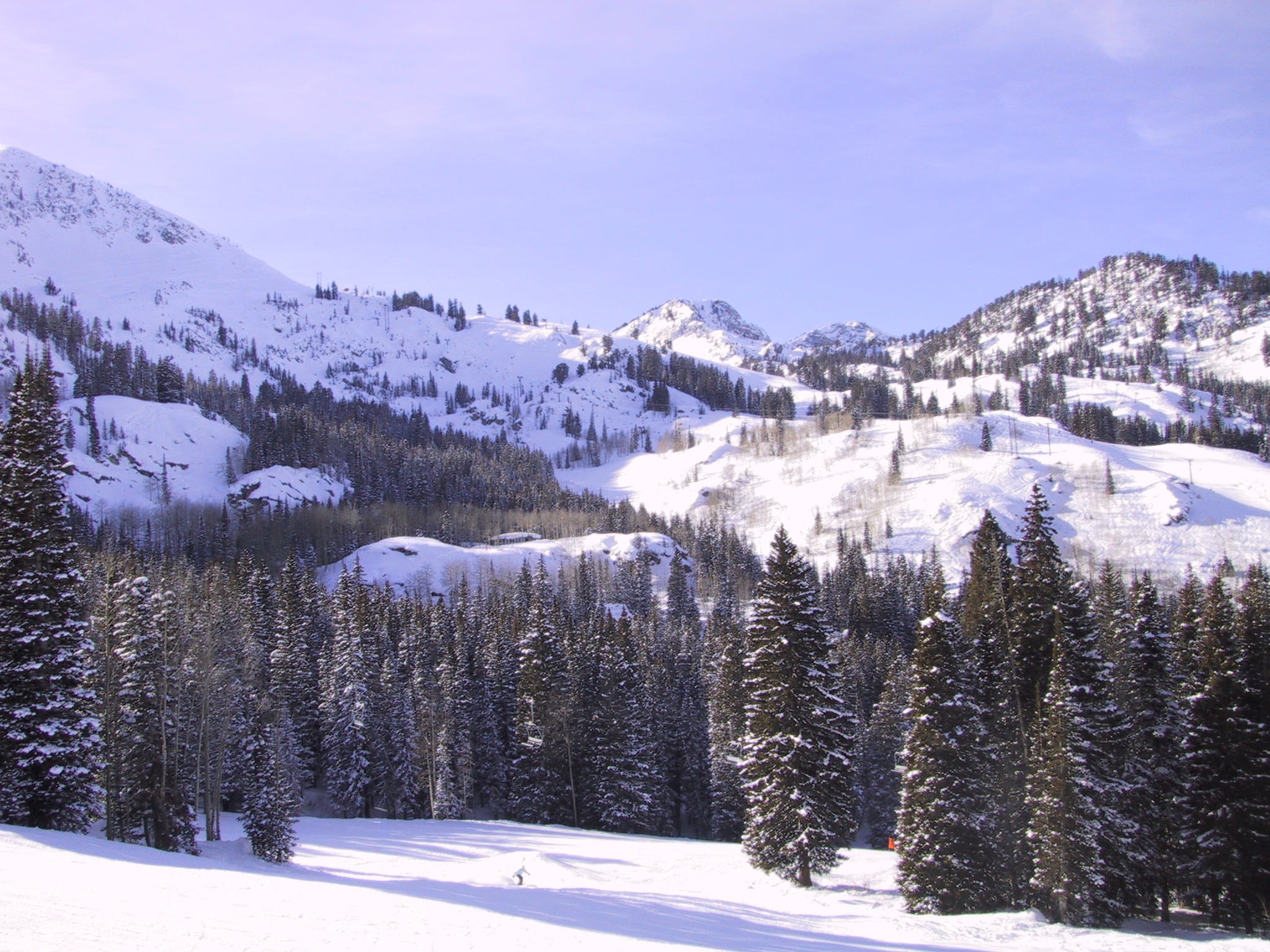 Snow-covered peaks and conifer-lined slopes above a groomed run at a Wasatch ski area