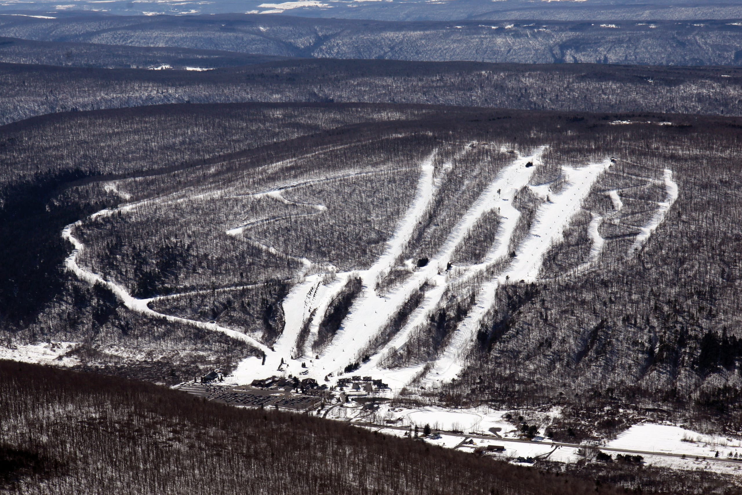 Aerial view of a wooded hill with white ski trails and a base area at its foot