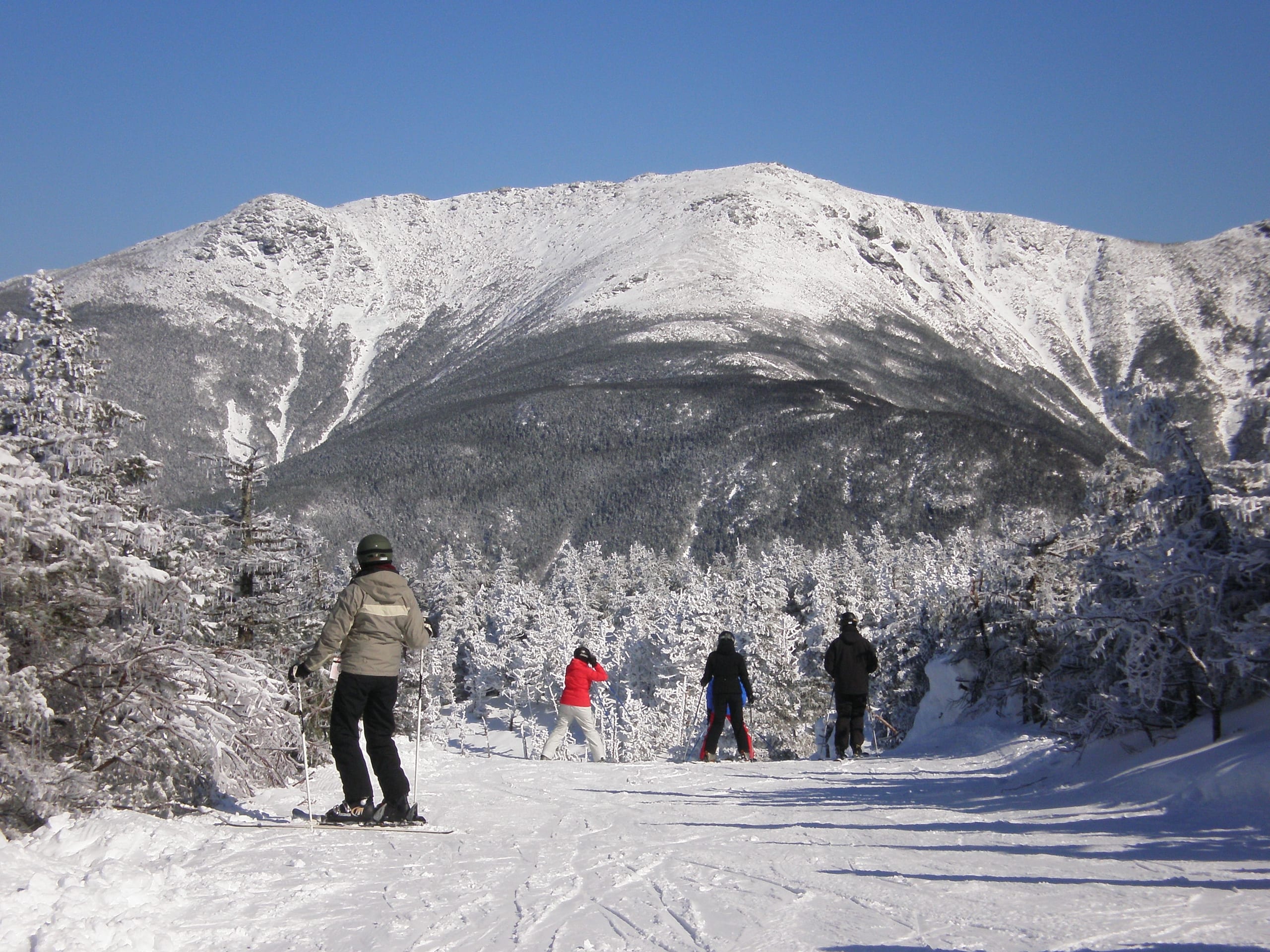 Skiers on a snowy trail at Cannon Mountain with Mount Lafayette's ridge across the valley