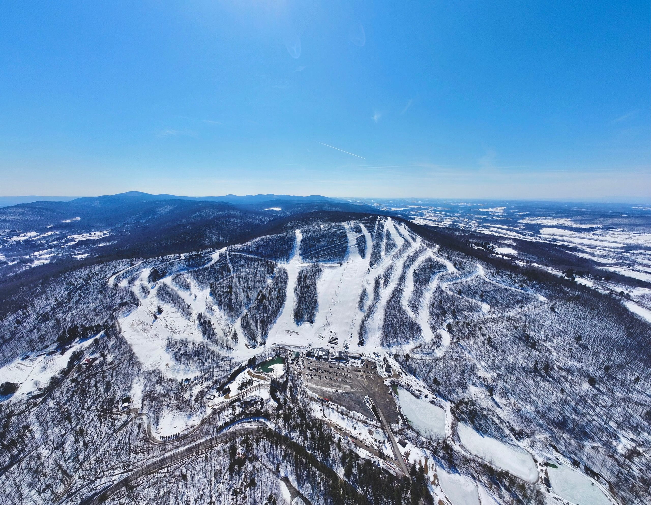 Aerial winter view of Catamount Mountain Resort's snow-covered trail network and base area on a forested ridge.