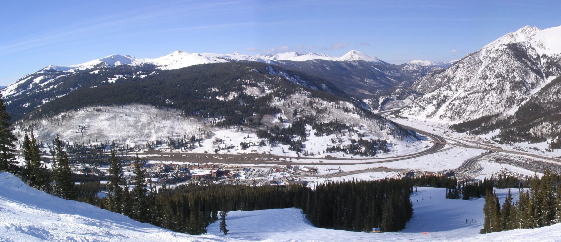 Panorama looking down a ski run to Copper Mountain's base village, I-70 and snowy peaks beyond