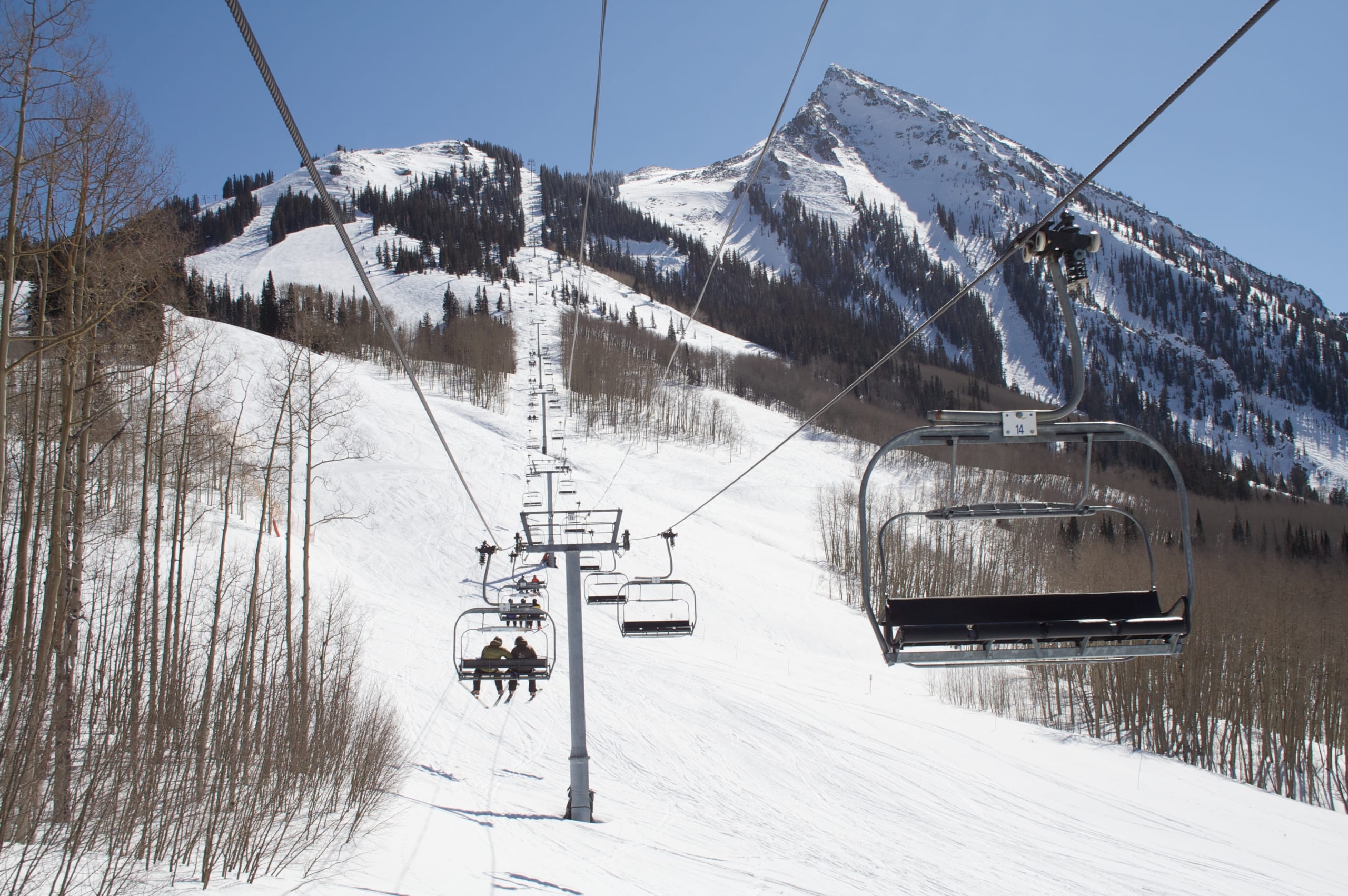 View from a chairlift up a snowy run toward Crested Butte's peak, with lift chairs and cables in frame