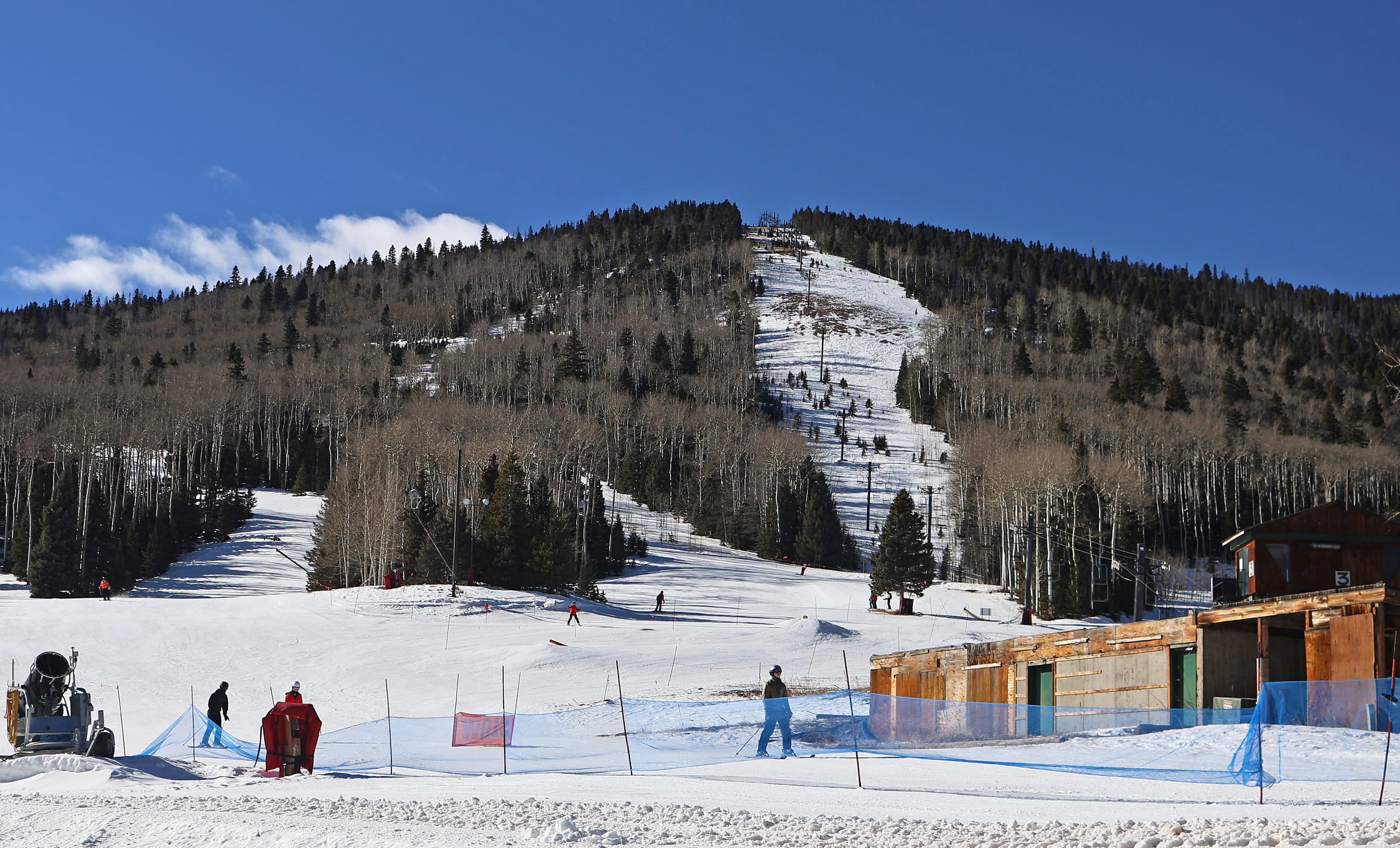 Snow-covered beginner slope and lift line rising to a forested ridge at Cuchara Mountain Park, with skiers and a base building