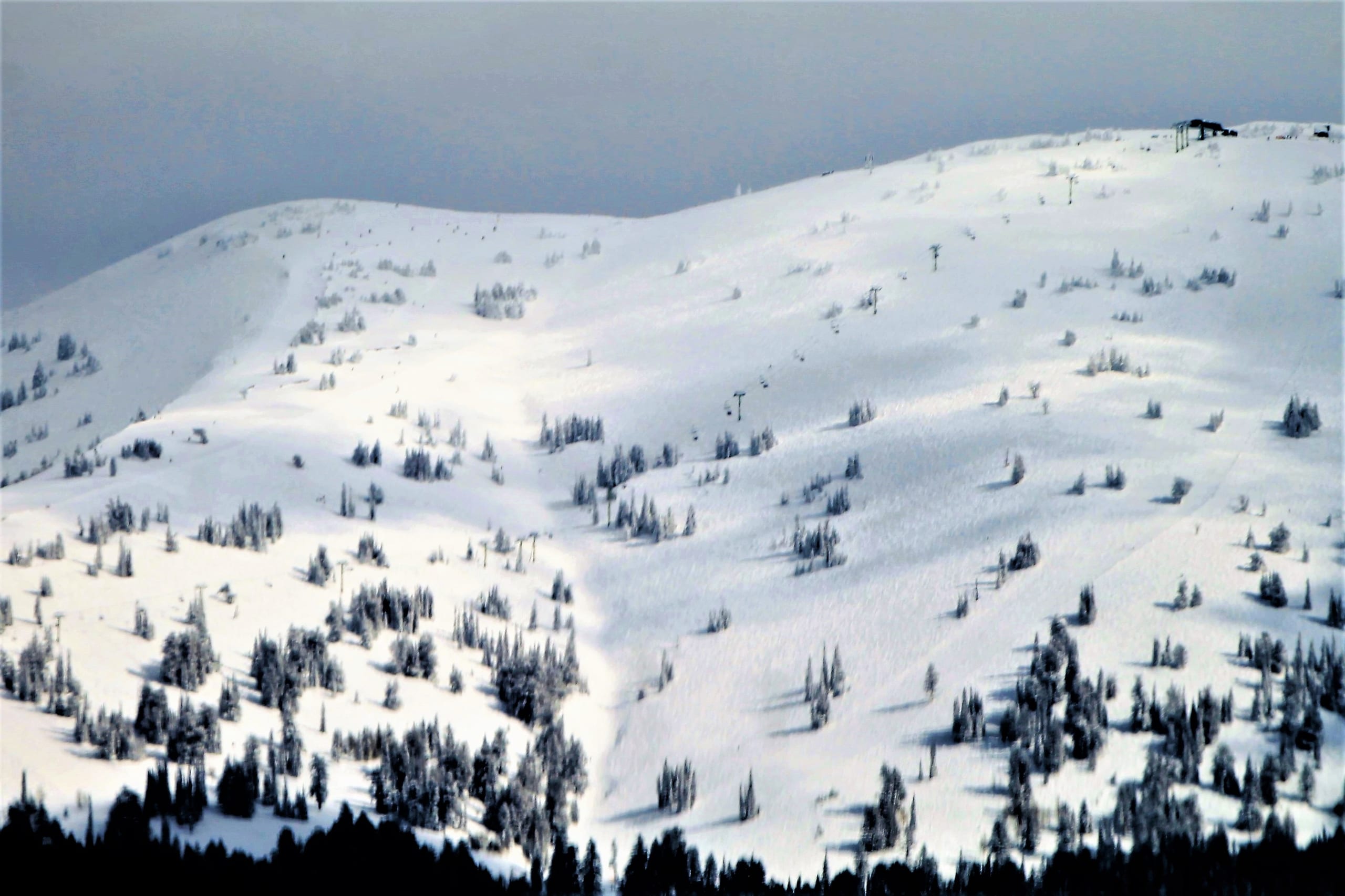 Snow-covered open ski slopes with a chairlift line and a summit building on the ridge