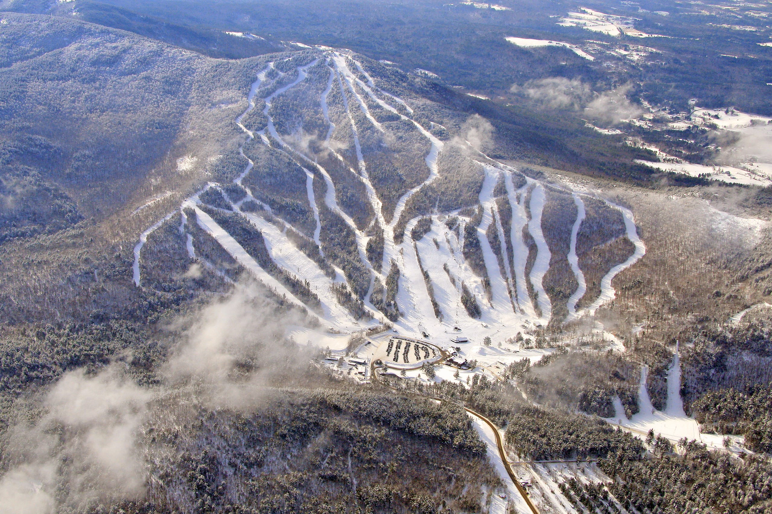 Aerial view of a snow-covered ski mountain with trail network, base lodge and parking below