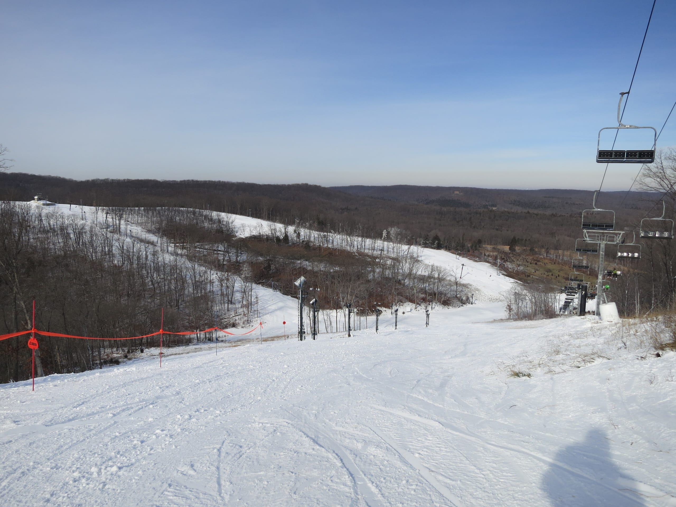 Snow-covered ski runs and a chairlift line descending toward wooded rolling hills under a clear sky