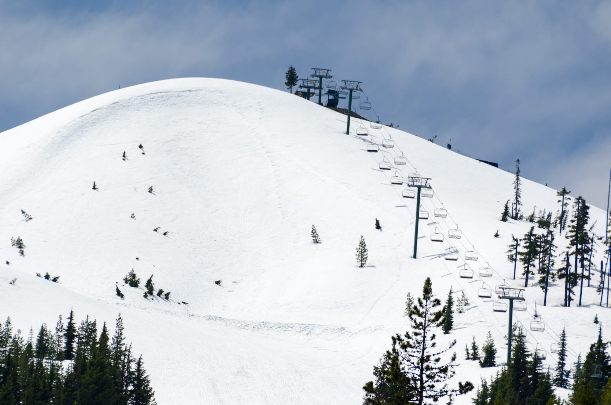 Snow-covered ski hill with a chairlift line climbing to the summit through scattered conifers