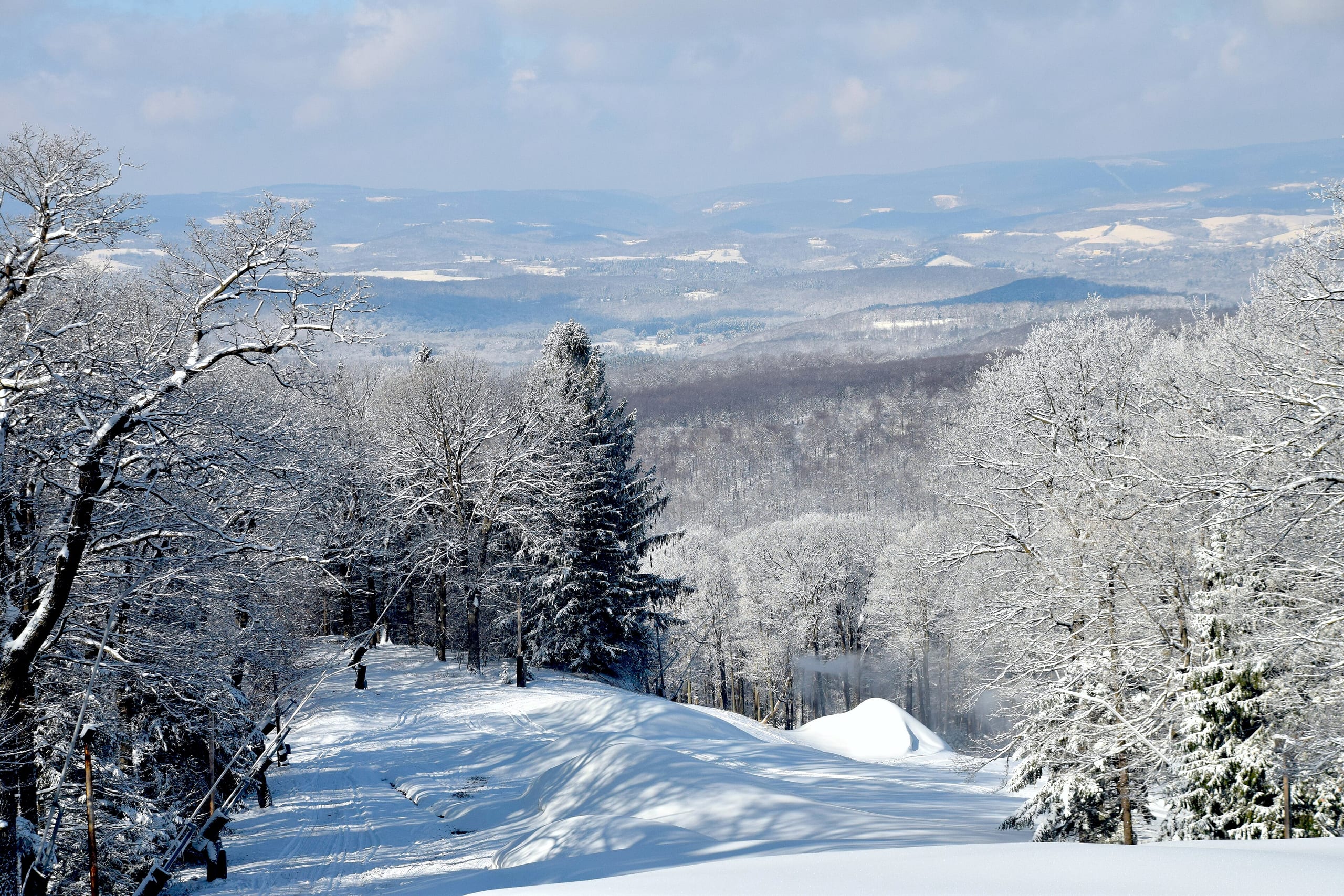 Snow-covered ski trail dropping through frosted trees with ridges of the Laurel Highlands beyond