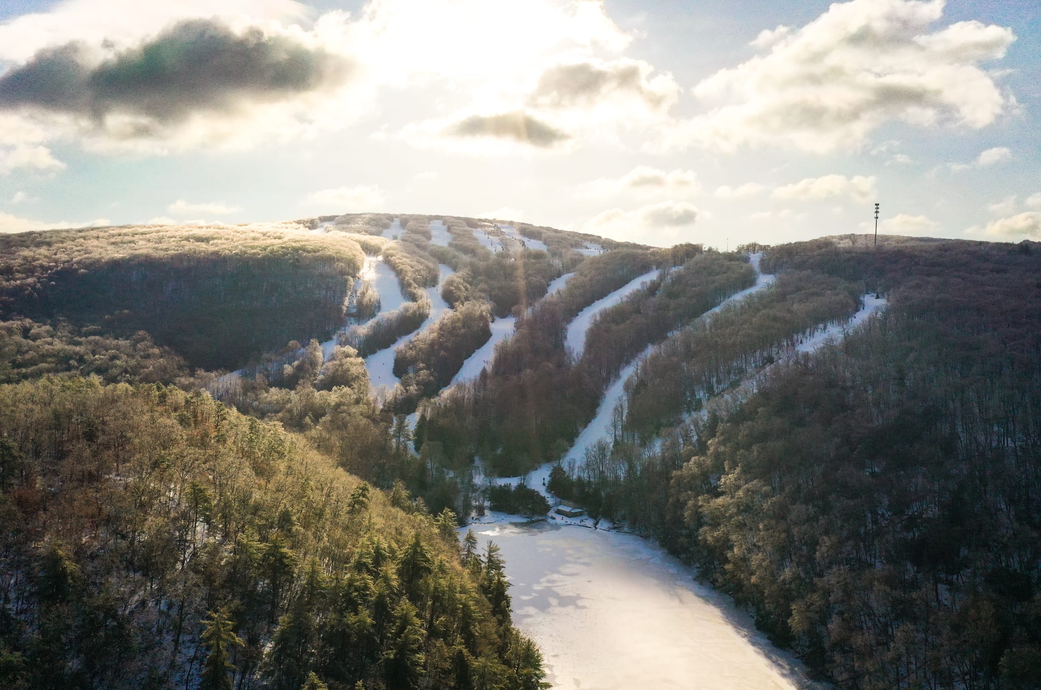 Aerial view of snow-covered ski trails cutting through wooded ridges above a frozen pond