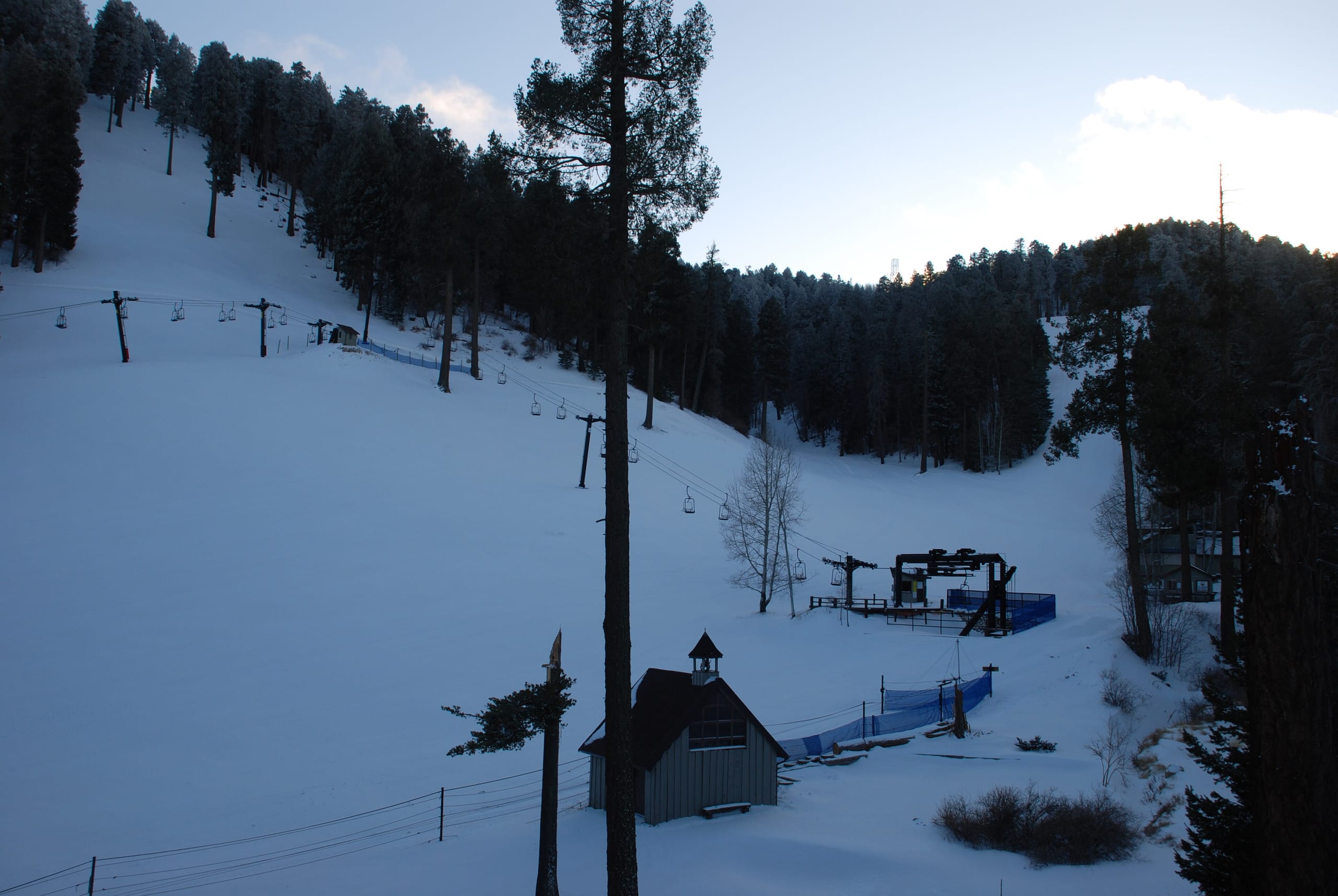 Snow-covered run and chairlift with base terminal and small building among pines at Mount Lemmon Ski Valley