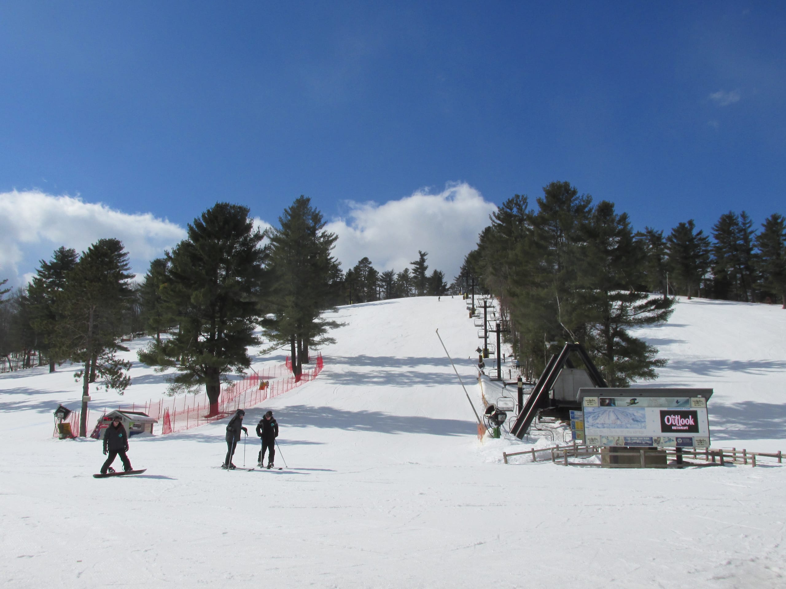 Snow-covered slope with a lift, pines and a few skiers at Nashoba Valley Ski Area, Westford, Massachusetts