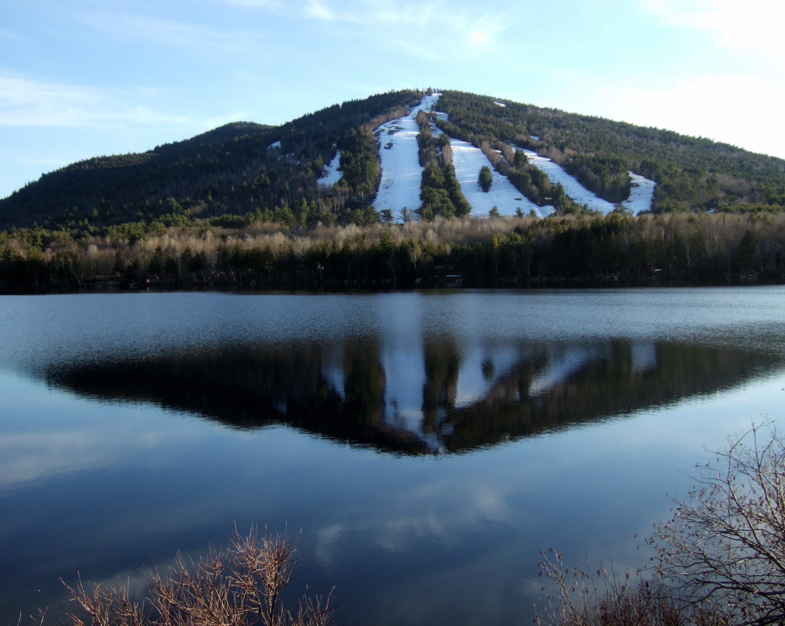 Pleasant Mountain's snow-streaked ski trails rise above Moose Pond, mirrored in the calm water.