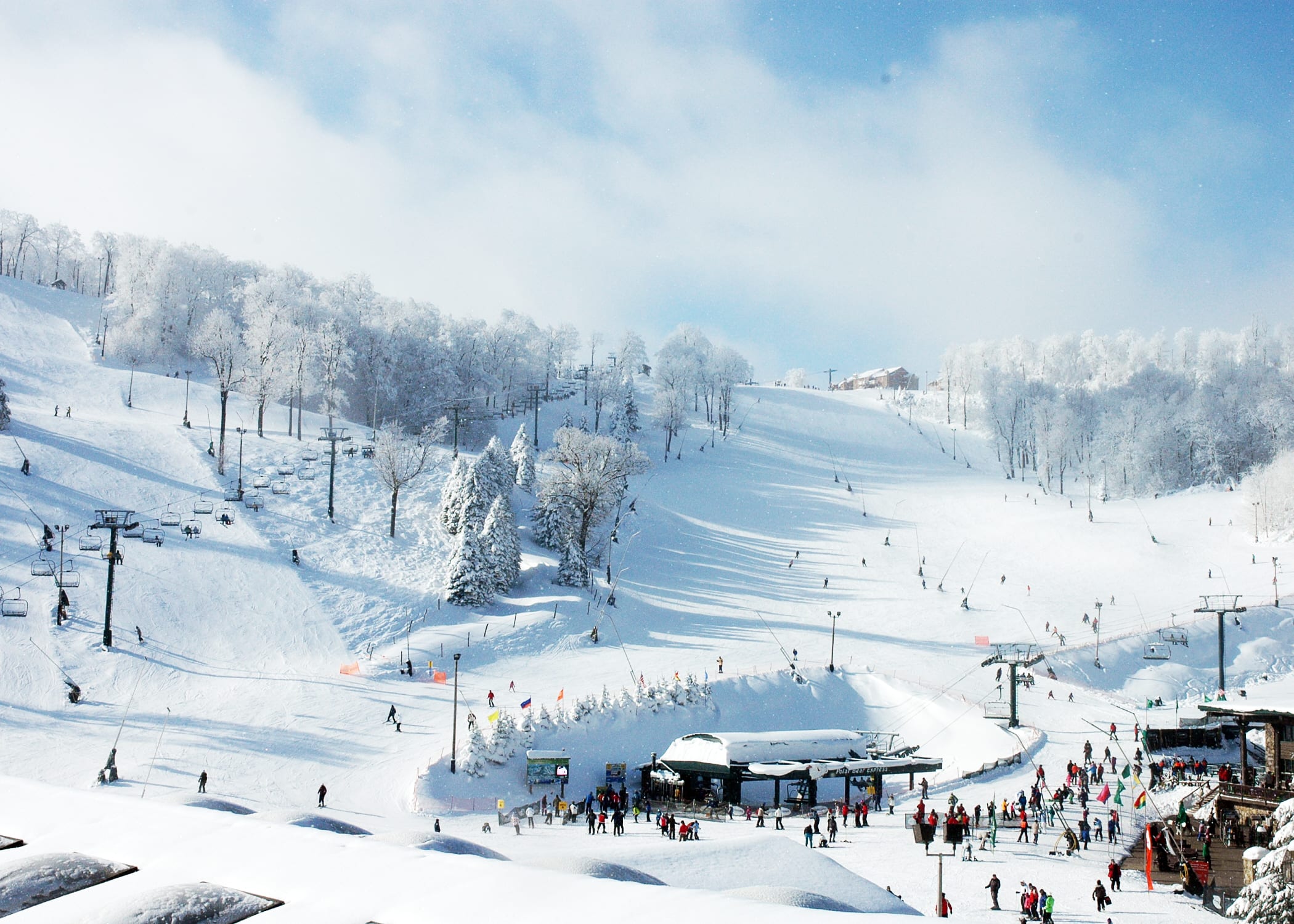 Snow-covered ski slopes with chairlifts, base lift terminal and many skiers at Seven Springs