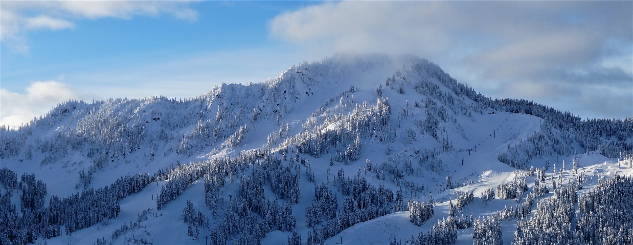Snow-covered Cowboy Mountain at Stevens Pass with cut ski runs and lift line on the right