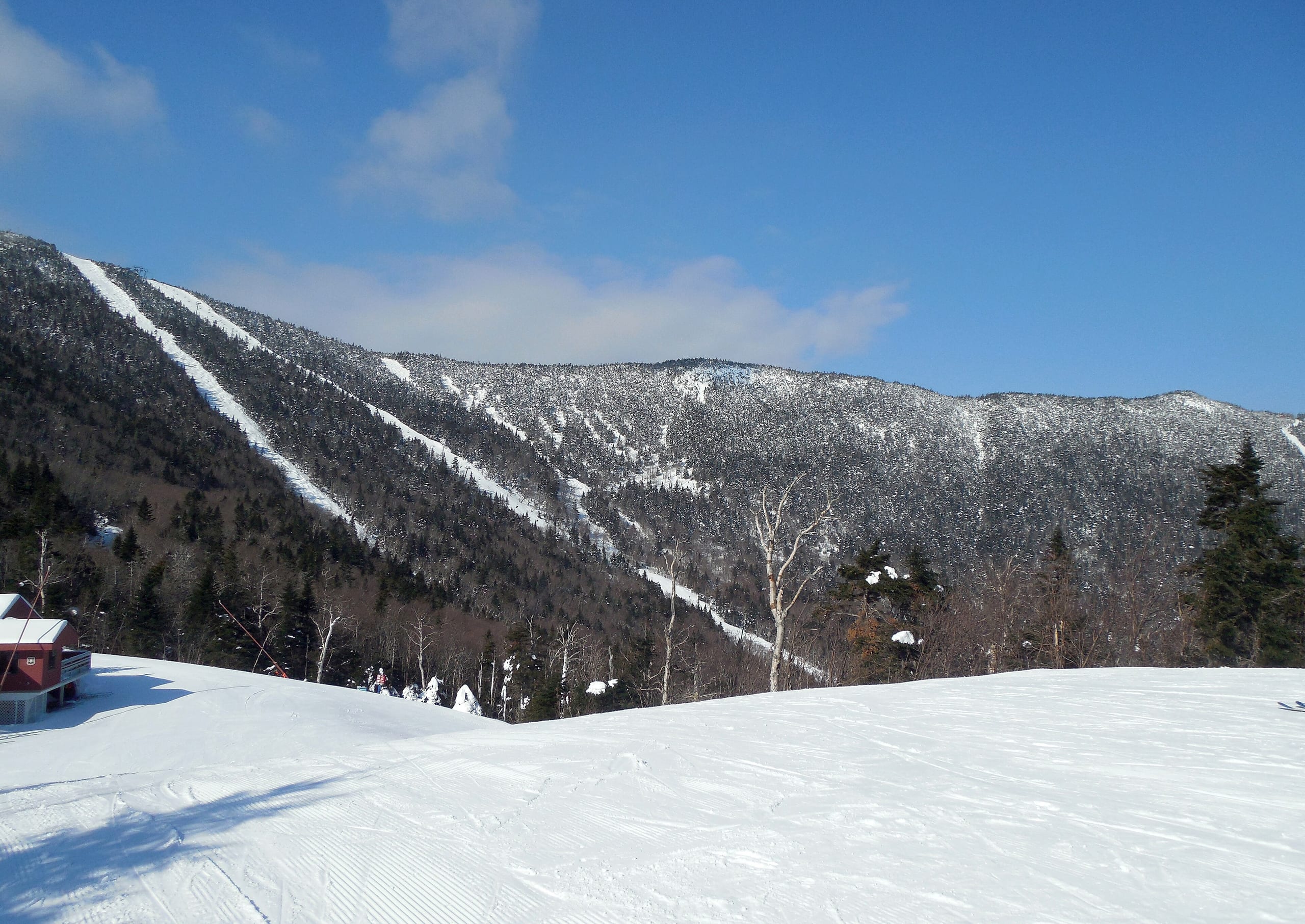 Groomed snow in the foreground with a snow-covered ridge cut by ski trails across a valley, Vermont