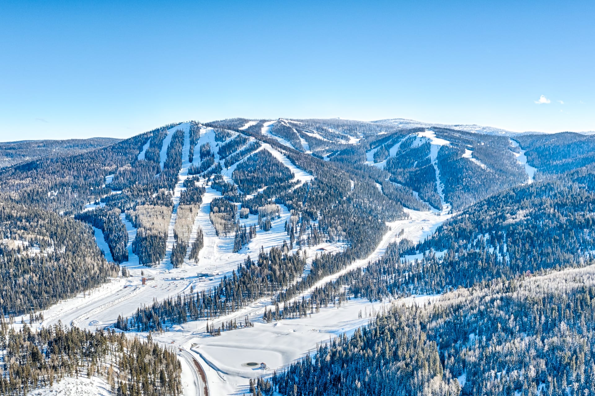 Aerial view of snow-covered ski runs and base area across three forested peaks at Sunrise Park Resort