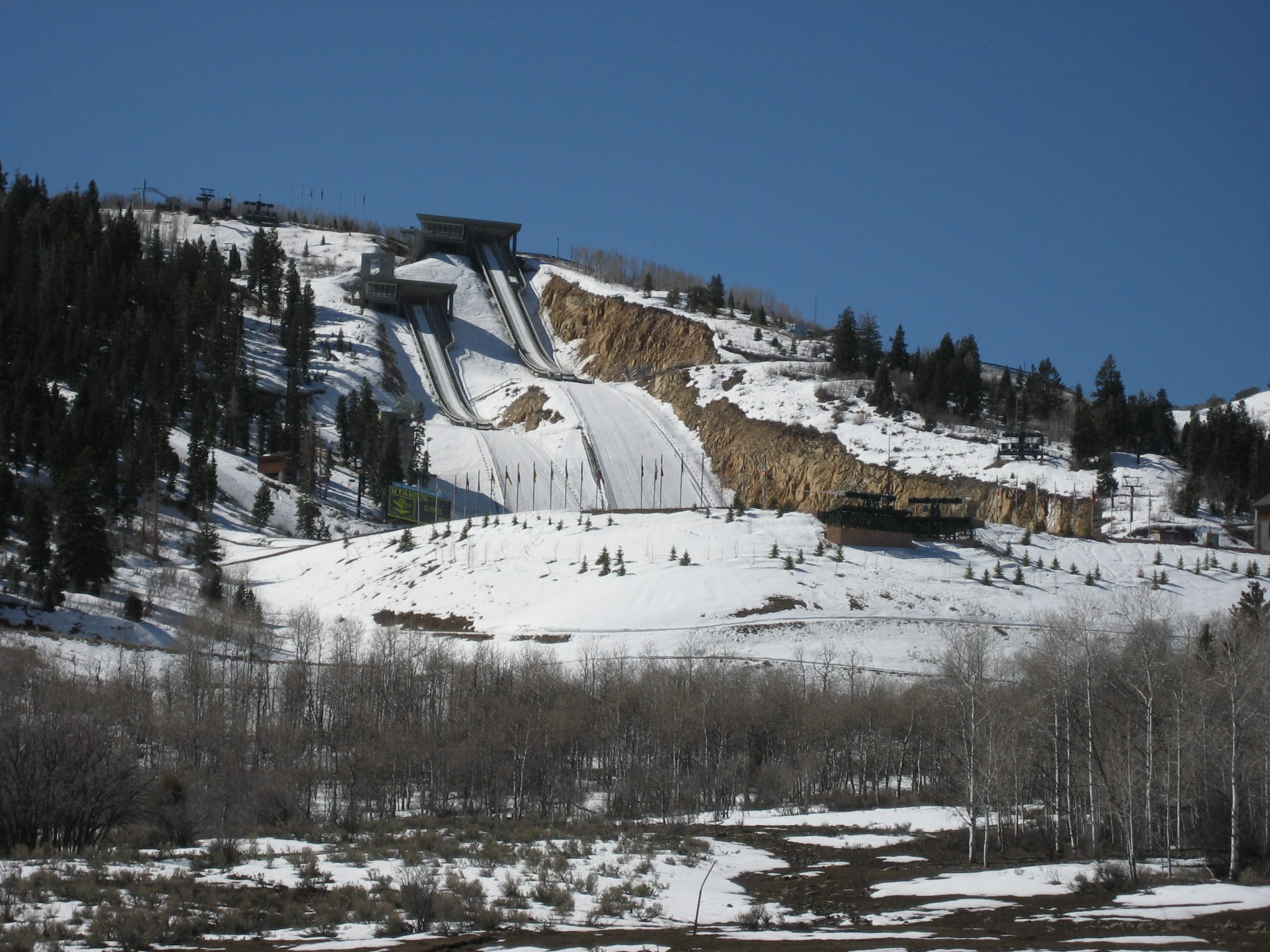 Ski jump towers and snow-covered inruns on a hillside at Utah Olympic Park, with bare aspens below