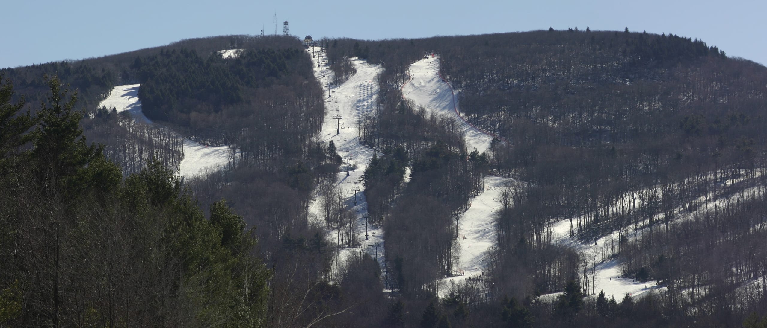 White ski trails and a lift line cut through bare winter woods on Wachusett Mountain, summit towers above.