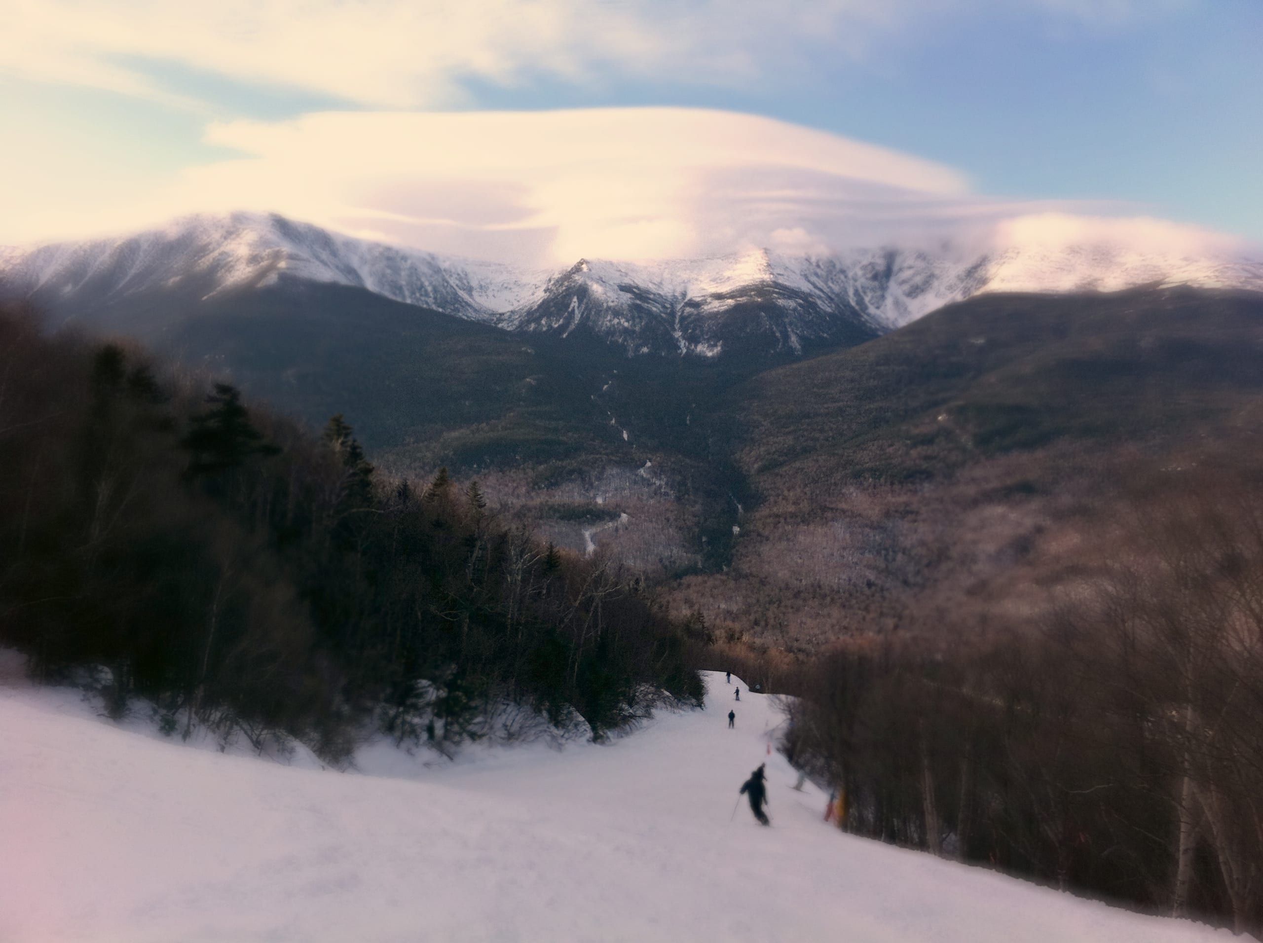 Skiers descend a snowy trail at Wildcat Mountain with Mount Washington and Tuckerman Ravine beyond