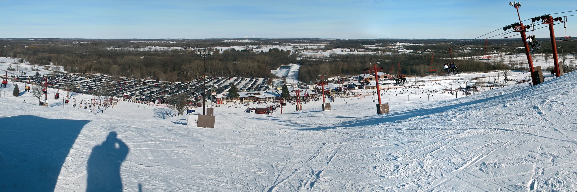Panorama from the top of Wilmot Mountain looking over snowy slopes, lifts and a full parking lot below