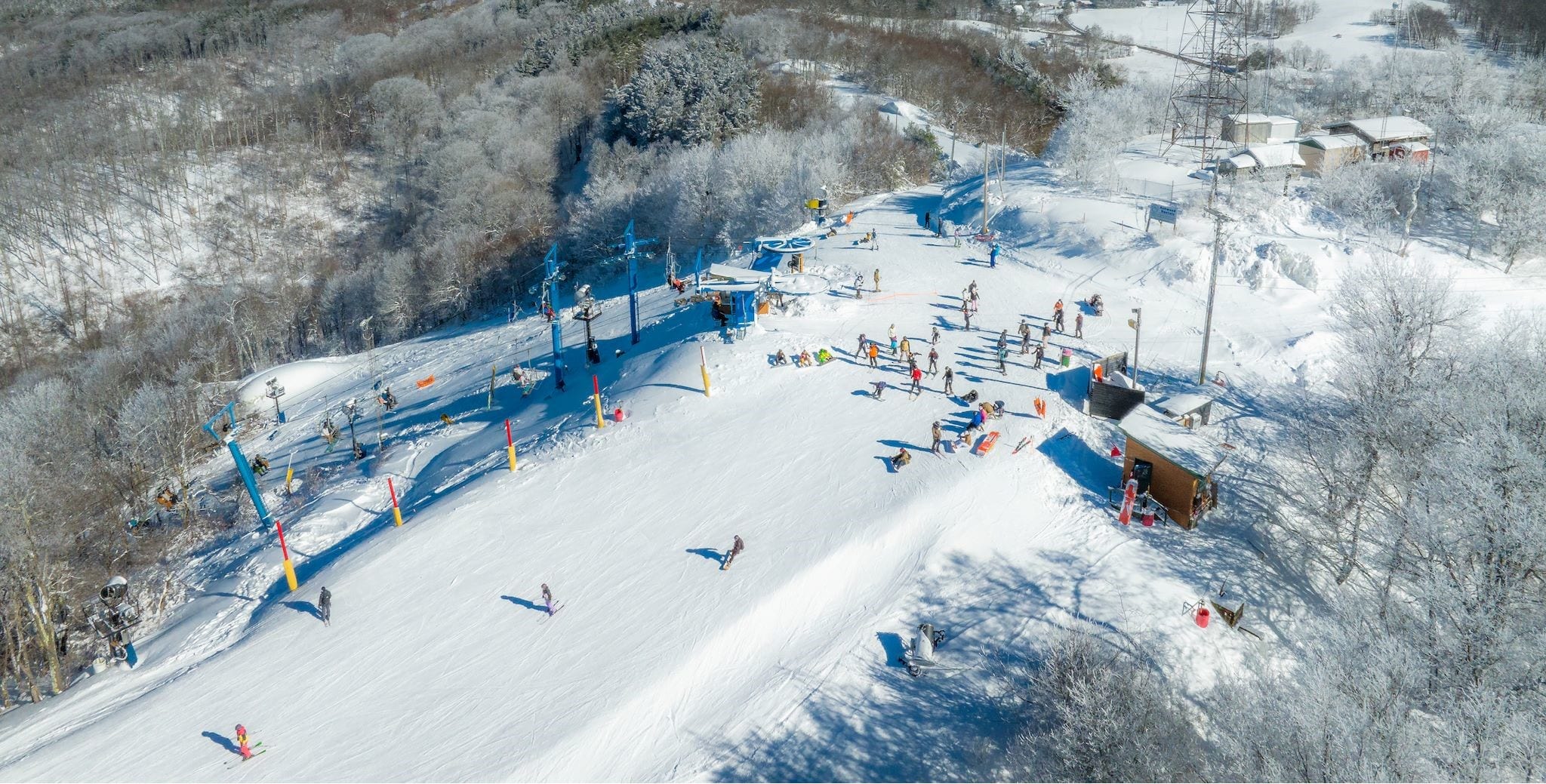 Aerial view of snow-covered ski slopes with a chairlift and skiers at a wooded hilltop