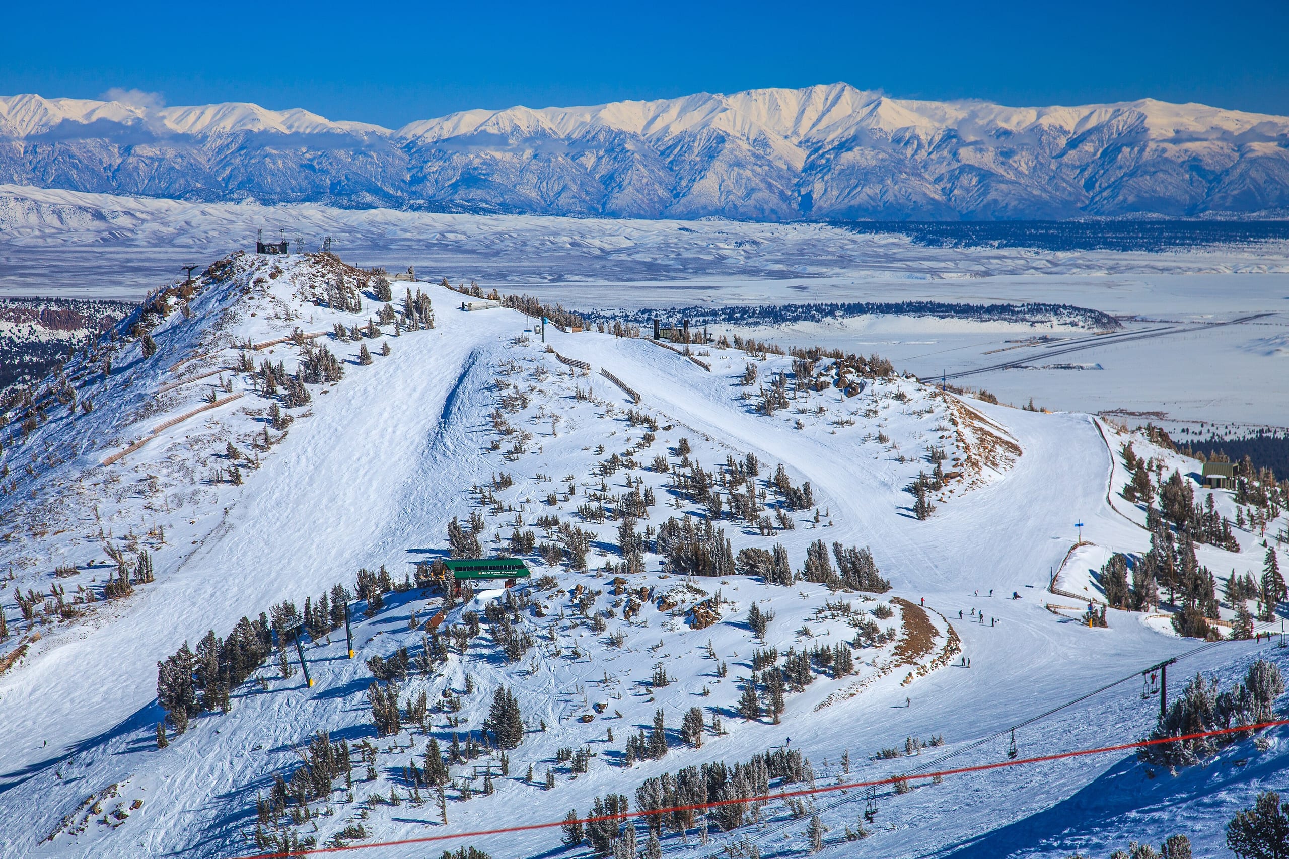 Snow-covered ridge and groomed runs at Mammoth Mountain with lifts and a distant valley and range beyond