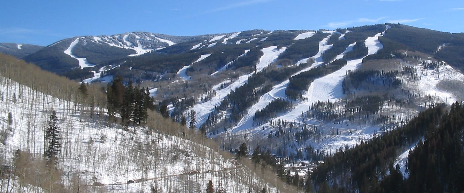 Snow-covered ski runs and glades on Vail Mountain's front side, seen across a valley under a clear sky.