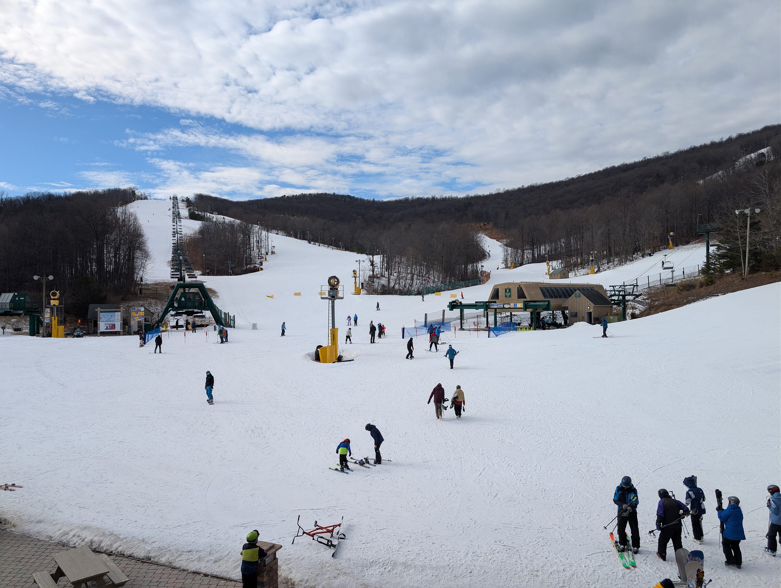 Skiers at the snow-covered base area of Whitetail Resort with two quad lifts and runs rising into bare winter woods